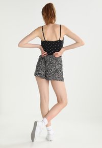 Débardeur noir à pois avec bretelles fines, associé à un short à motifs multicolores. Modèle portant des baskets blanches, vu de dos.