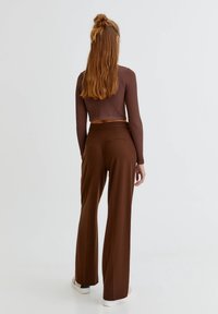 Bruin geribbeld crop top gecombineerd met hoge taille bruine broek. De broek heeft een achterzak, een gladde textuur en een vloeiende snit.