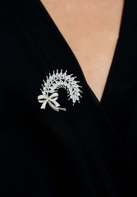 Spilla d'argento a forma di foglia stilizzata, con pietre trasparenti tagliate a marquise e un accento a fiocco. Posizionata su un indumento nero.