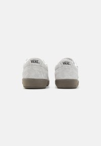 Sivé semišové tenisky s nízkym dizajnom, ktoré majú hnedú gumovú podrážku a čierne logo Vans na päte. Čistý a minimalistický štýl.