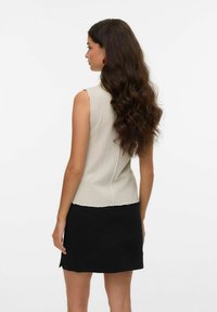 Un haut sans manches à côtes gris clair avec une couture latérale et un ourlet brut, associé à une mini jupe noire. De longs cheveux ondulés tombent dans le dos.