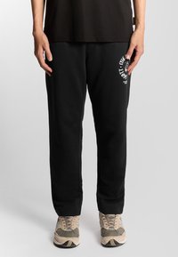 Zwarte joggingbroeken met een relaxed fit, voorzien van een wit grafisch logo op de linkerdij. Zachte stof met een gladde textuur en een elastische tailleband.