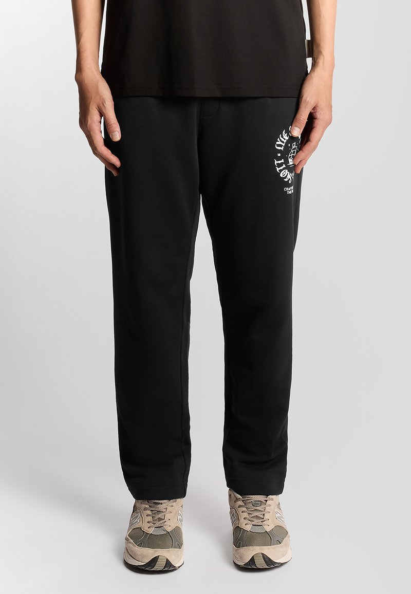 Zwarte joggingbroeken met een relaxed fit, voorzien van een wit grafisch logo op de linkerdij. Zachte stof met een gladde textuur en een elastische tailleband.