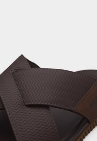 Sandale marron avec brides croisées texturées et semelle souple, conçue pour un usage décontracté.