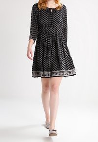 Vestido negro con estampado, cuello redondo, mangas tres cuartos y cintura elástica, con un dobladillo contrastante y divertidos diseños geométricos.