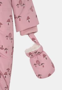 Chaqueta infantil rosa con patrón de setas y forro de felpa suave, presentada en la manga y la correa del mito sobre un fondo blanco.