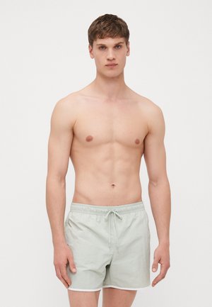 Costumi da bagno verde chiaro realizzati in tessuto leggero, caratterizzati da una vita elastica con cordino e dettagli bianchi all'orlo.