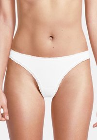 Perizoma bianco realizzato in morbido tessuto, con rifiniture in pizzo lungo l'elastico in vita e le aperture delle gambe, caratterizzato da un design semplice e minimal.