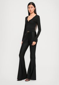 Black fitted long-sleeve top with a V-neck and gold ring detail. Paired with flared black pants featuring a shiny texture and gold belt accent.
