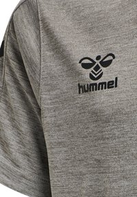 Grå atletisk t-shirt med en strukturerad stickad design, med en svart "hummel"-logotyp och bi-emblem på vänster sida.