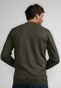 Groene gebreide trui met een ronde halslijn, geribbelde manchetten en zoom. Het materiaal lijkt zacht met een gladde textuur en heeft een effen kleur.
