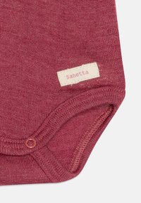 Body in rosso scuro, tessuto a maglia morbido. Presenta un'etichetta con "Sanetta," un collo rotondo e chiusure a scatto nella parte inferiore.