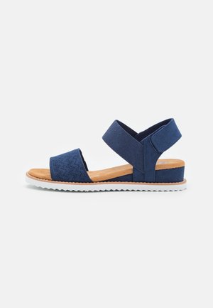 Marineblauwe sandaal met open teen, gevoerd met een zacht beige voetbed, elastische enkelband en een witte profielzool, ideaal voor casual gebruik.