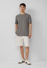 T-shirt en coton gris à manches courtes, col rond et détails en patch subtil ; associé à un short blanc jusqu'au genou et des baskets blanches.
