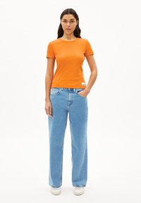 Oranje, kort mouw ribbed t-shirt gecombineerd met lichtblauwe, losse spijkerbroek. Witte sneakers maken de outfit compleet.