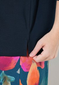 Marineblaues Baumwoll-T-Shirt mit einem Seitenschlitz-Detail, kombiniert mit auffällig bunten Shorts mit Blumenmuster in Pink, Orange und Türkis.
