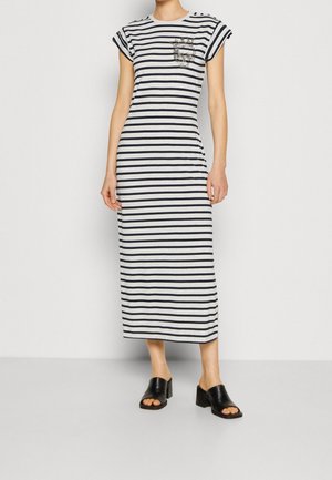 Femme portant une robe midi à rayures horizontales noires et blanches avec des manches courtes et des sandales noires à talons ouvertes à l'avant.