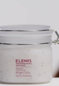 ELEMI Frangipani Monoi Salt Glow, 490 g burk. Transparent glas med silvermetallclip, vit skrubb synlig, med bruna flingor.