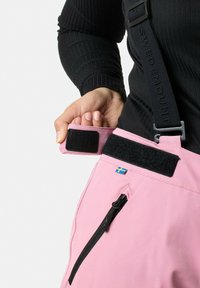 Pink pants with black Velcro fastener, side zip pocket, and a small blue and yellow flag. Adjustable straps with visible branding.