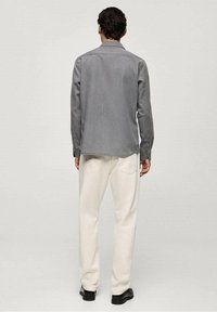 Graues langärmliges Hemd mit gerader Passform, leicht strukturiertem Stoff und Knopfmanschetten, kombiniert mit cremefarbenen Schlaghosen.