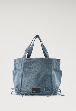 Sac fourre-tout en denim bleu avec deux anses, poches latérales, détails à nouer aux coins inférieurs, et une étiquette noire portant l'inscription "KARL LAGERFELD JEANS".