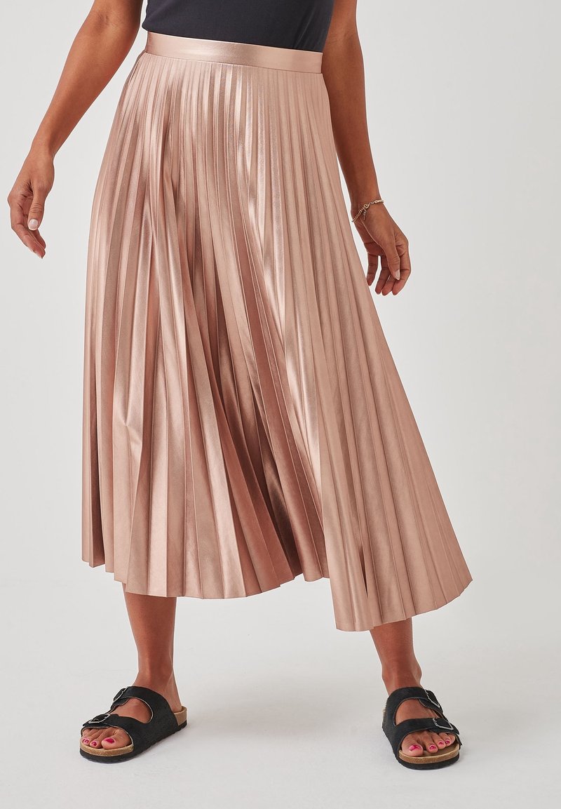 Plissé midi rok in zacht roze satijn, met een hoge tailleband, glanzende afwerking en een vloeiende silhoutte. Gecombineerd met zwarte sandalen.