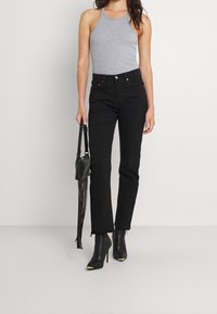 Top a fascia grigio, jeans neri a vita alta con orlo sfilacciato, abbinati a stivaletti neri con tacco e dettagli dorati e una piccola borsa nera.