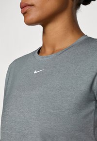 Camiseta atlética gris hecha de material suave, con un cuello redondo y un pequeño logo blanco de Nike en el pecho.