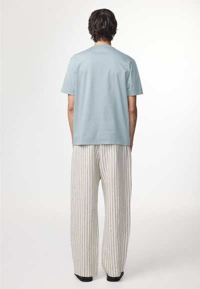 Lyseblå kortærmet t-shirt sat sammen med stribede brede bukser. Bukserne har lodrette marineblå striber på en cremefarvet bund.