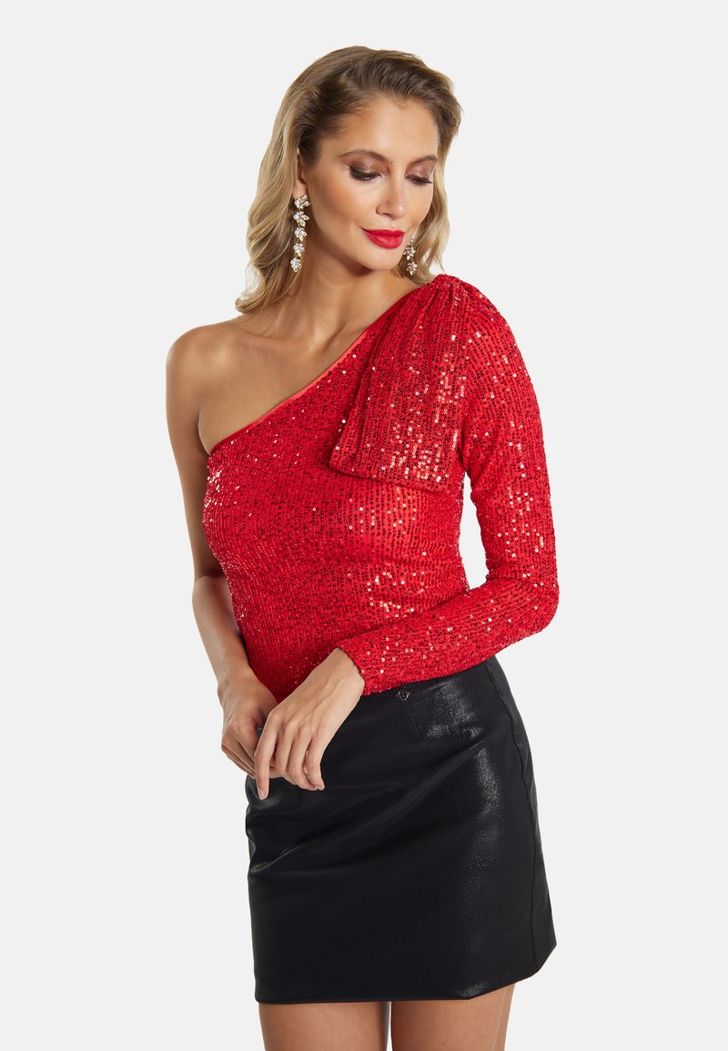Top rosso di paillettes con design a spalla unica, decorato con un dettaglio a fiocco in tessuto sulla spalla, abbinato a una mini gonna nera aderente.