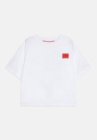 Camiseta de algodón de manga corta blanca con un parche rectangular rojo que dice "HUGO" en el lado izquierdo del pecho. Diseño de cuello redondo.