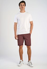 T-shirt bianco a maniche corte, pantaloni corti a quadri bordeaux con risvolti, e sneakers bianche con dettagli colorati. Outfit semplice e informale.