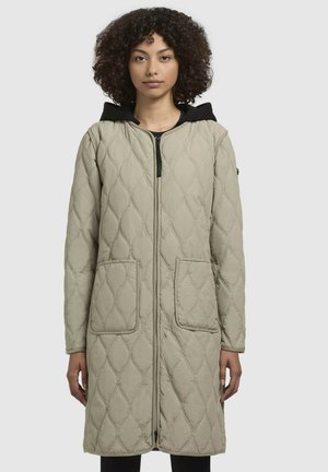 Gequilte lange jas in lichtbeige, met een zwarte capuchon, vooraan met een ritssluiting en twee grote zakken. Gladde textuur met een gemusterd ontwerp.