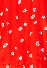 La tela roja presenta un estampado floral con pequeñas flores blancas y lavanda, acentuado por hojas verdes, en una textura suave y ligera.