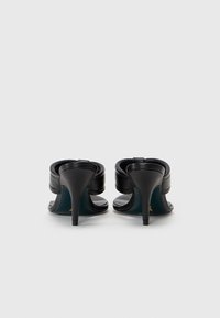 Svarta klackade sandaler med en slät läderöverdel, öppen bakdesign och böjda remmar. Klackhöjden är cirka 7,5 cm.