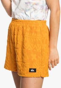 Pomarańczowe szorty z frotté o teksturowanym kwiatowo-geometrycznym wzorze, elastyczna talia i mała metka marki z boku.