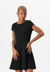 Robe noire à manches courtes avec un corsage ajusté et une jupe évasée, présentant des détails de coutures subtils et une texture de tissu lisse.