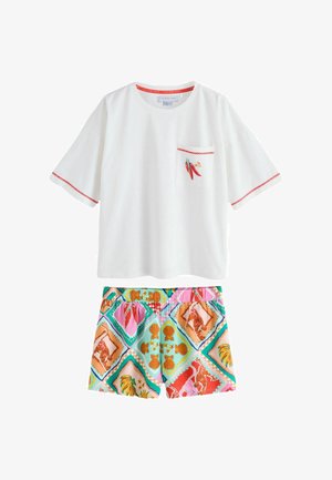 Biała koszula z krótkim rękawem z drobną haftowaną papryczką chili na kieszeni i czerwonym wykończeniem, zestawiona z kolorowymi spodniami szortami w motywy muszli morskich.