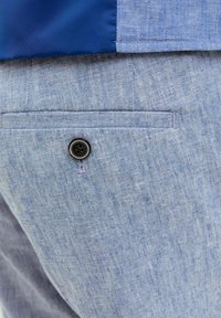 Pantaloni personalizați de culoare bleu deschis, confecționați dintr-un material texturat, având un buzunar la spate cu un nasture negru și cusături de contrast.