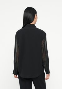 Zwarte lange mouwen shirt van een gemengde stof, met doorschijnende mouwen, een klassieke kraag en knoopmanchetten, ontworpen voor een losse pasvorm.