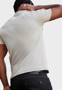 Beige polo paita, joka on pehmeä tekstiililtään ja klassiselta muotoilultaan, yhdistettynä tummiin farkkuihin, joissa on merkki takana ja kapea istuvuus.