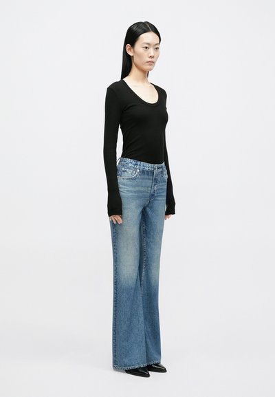 Top preto de manga comprida com decote redondo, combinado com jeans de ganga azul claro de perna larga, com lavagem desbotada e design clássico de cinco bolsos.