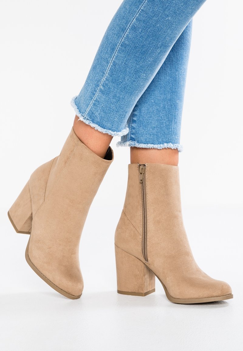 Bottines en daim marron clair avec talons carrés et fermetures éclair latérales, portées avec un jean skinny bleu clair à ourlet effiloché.
