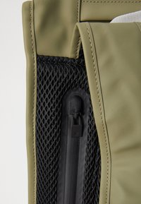 Borsa verde oliva con un pannello in rete nera texturizzata e una tasca con zip, con cuciture rinforzate lungo i bordi.