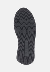 Suola di scarpe in gomma nera con un motivo a ondine e un'etichetta rettangolare "GUESS" al centro, che offre aderenza e grip.