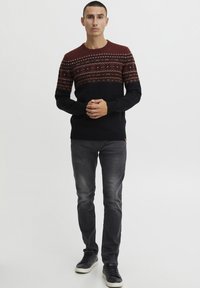 Svart genser med en burgunderfarget og mønstret yoke-design. Rund hals, ribbestrikkede mansjetter og nederkant. Grå jeans og svarte høyhælte sneakers fullfører antrekket.