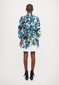 Blumenmuster-Kleid mit blauen, grünen und braunen Mustern; verfügt über einen gerafften Rock, lange Puffärmel und einen kragenloser Ausschnitt. Getragen mit schwarzen Knöchelboots.