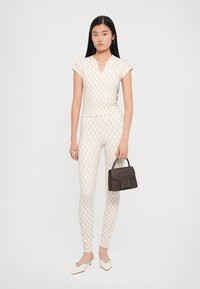 Aansluitend top en leggings in crème met een geometrisch patroon, aangevuld met een kleine bruine handtas en crème puntige schoenen.