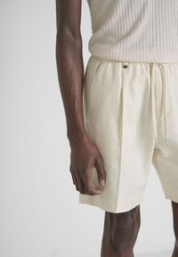 Pantaloni corti in lino giallo chiaro da uomo con pieghe laterali, vita elastica e dettaglio con coulisse. Tessuto testurizzato con vestibilità comoda.