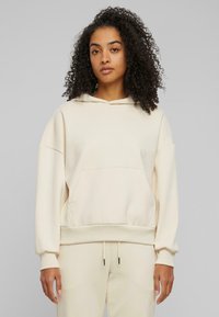 Haut à capuche beige avec une poche avant, un cordon de serrage et des poignets côtelés. Fabriqué en tissu doux, avec une coupe décontractée et une texture lisse.